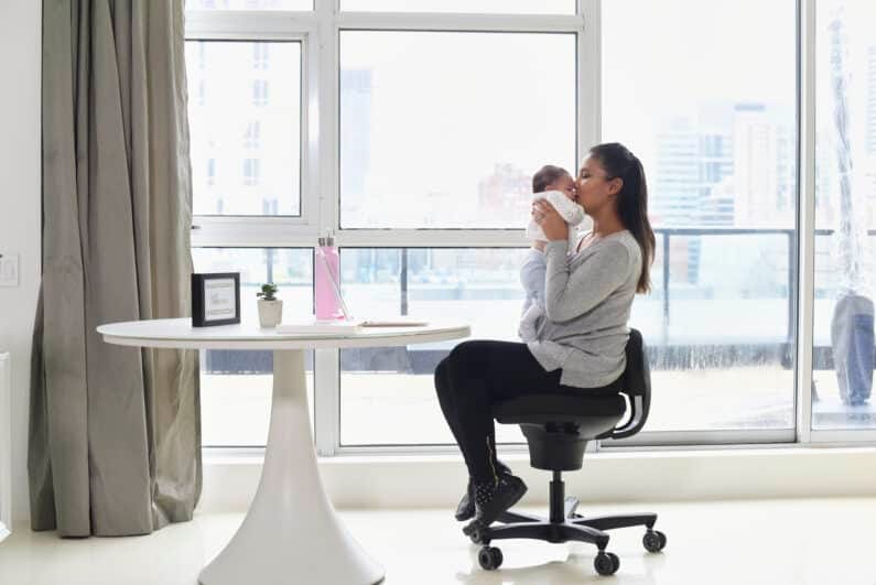Woman sitting in a CoreChair while she hugs and kisses her new born baby.
